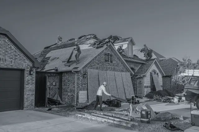 Roofing crew tearing off and replacing a roof on a brick house